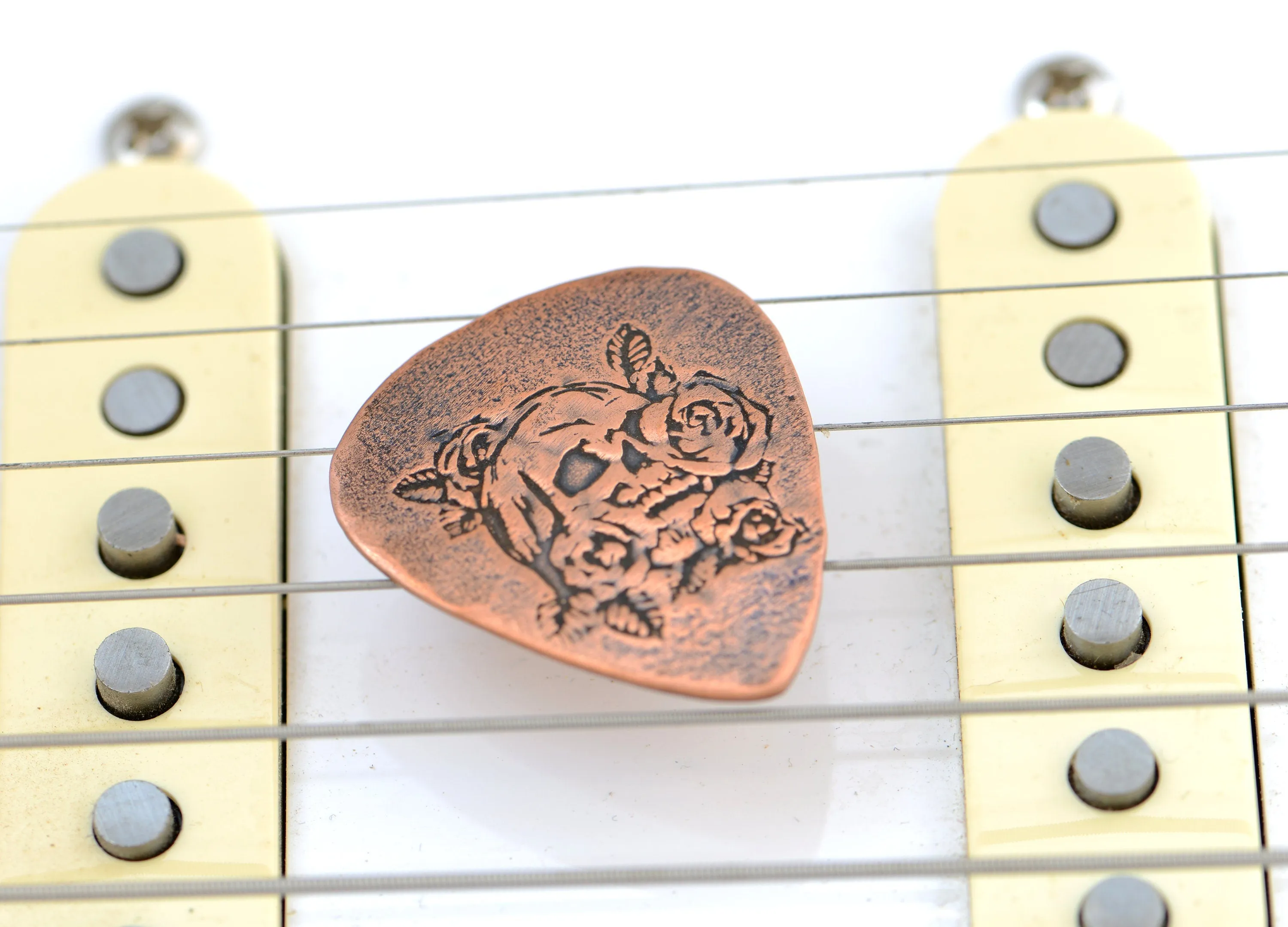 Guitar pick in copper with skull and roses