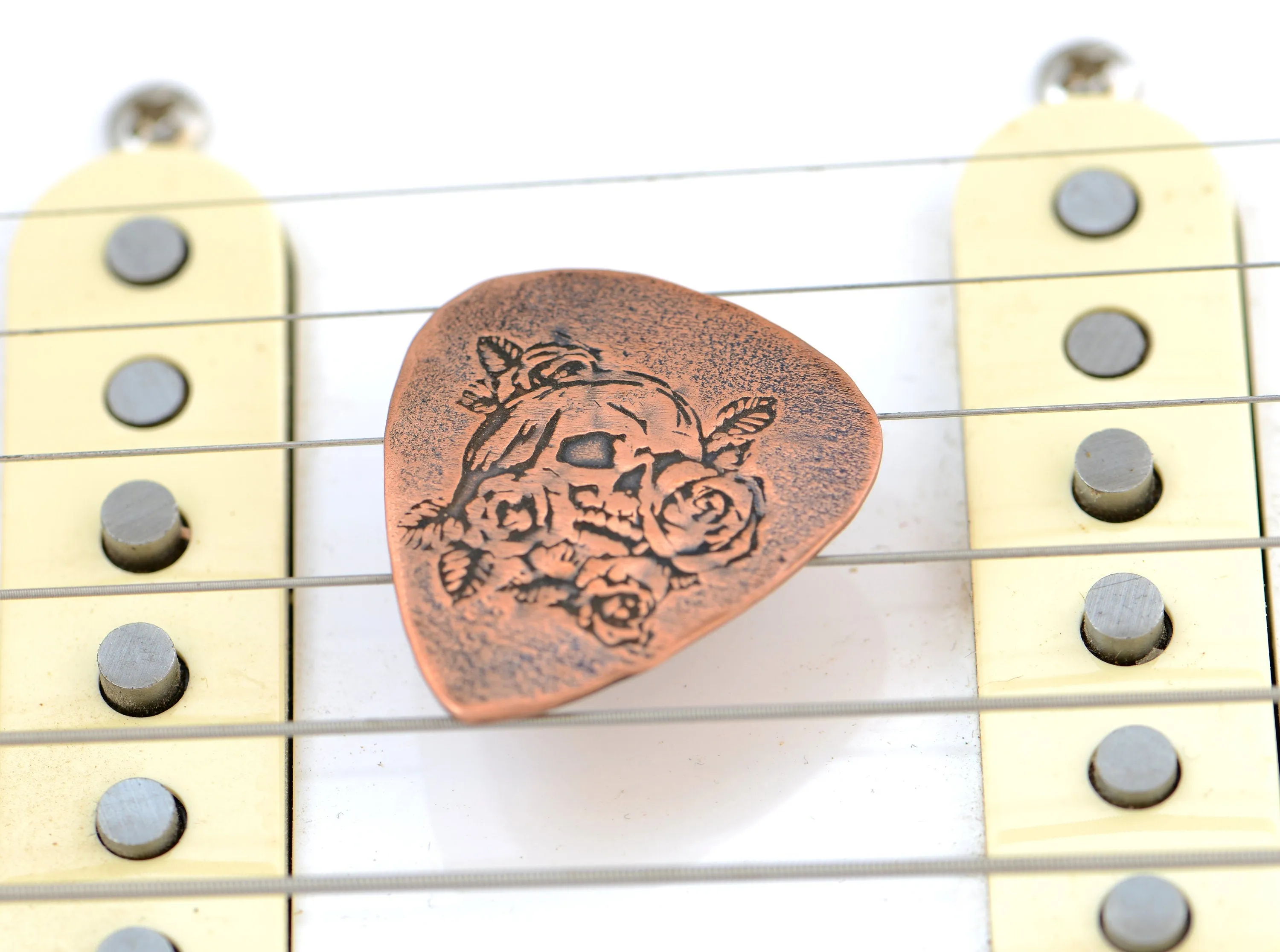 Guitar pick in copper with skull and roses