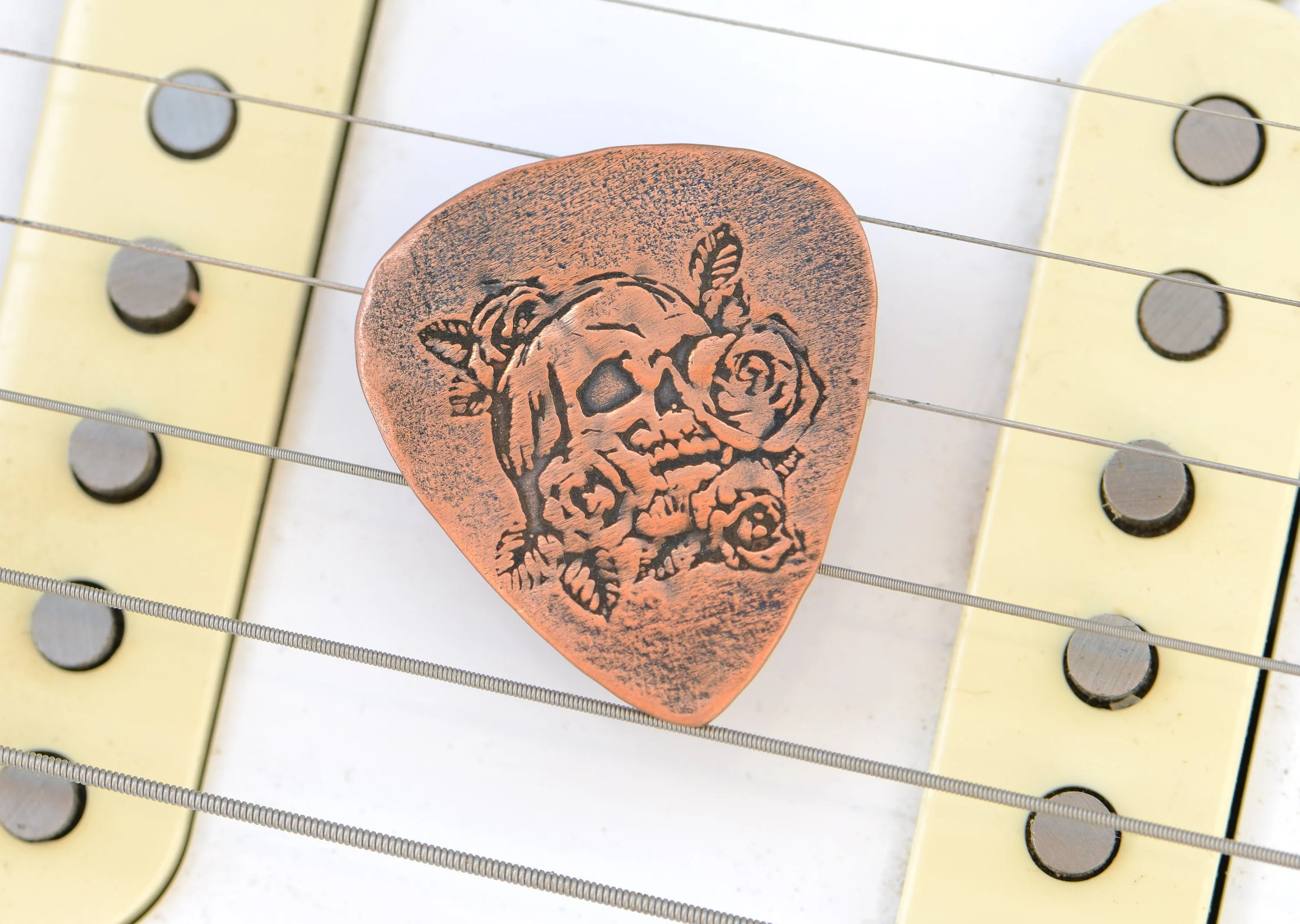Guitar pick in copper with skull and roses